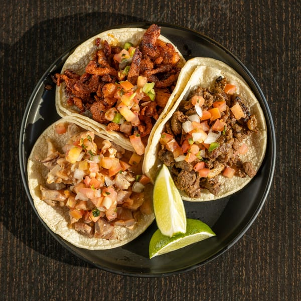 Three Mexican tacos with different meat fillings and pico de gallo, served with lime wedges.