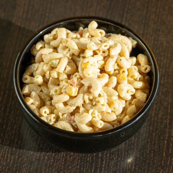 A black bowl filled with creamy macaroni salad, featuring elbow pasta, corn, and red bell pepper.