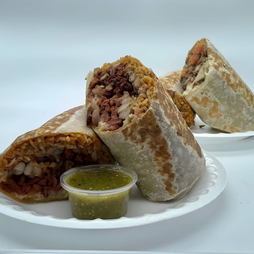 Three large, cut Mexican burritos filled with meat, rice, and beans, with a side of green salsa.