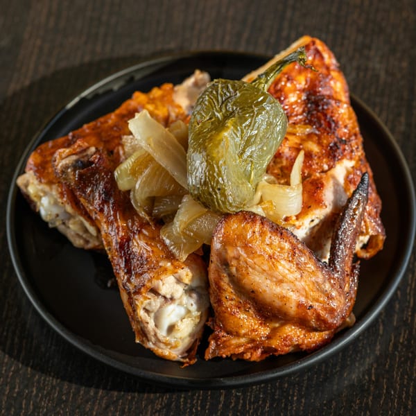 Grilled chicken with a roasted green pepper and caramelized onions on a black plate.