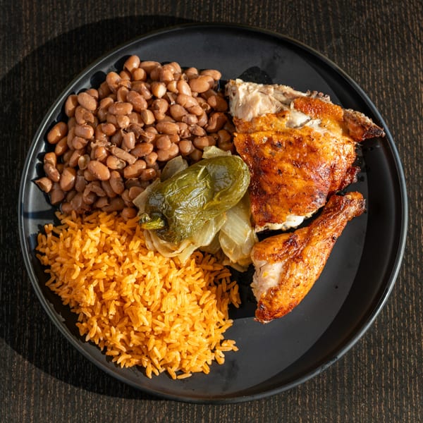 Señor Pollo's Mexican grilled chicken with rice, beans, and roasted peppers on a black plate.