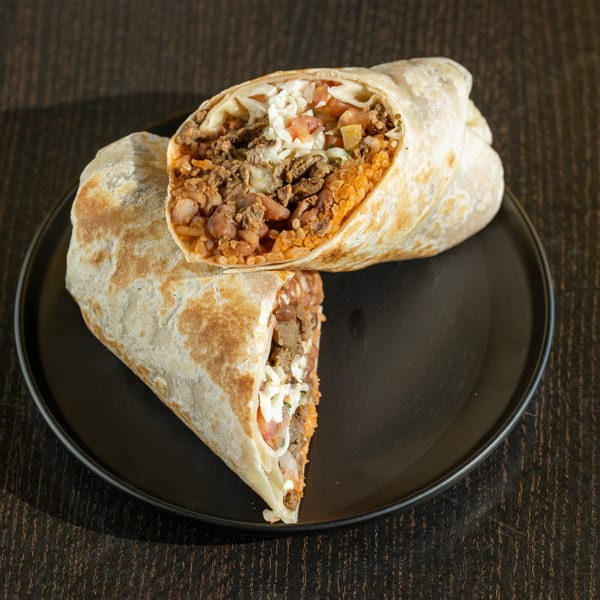 A large Mexican burrito, cut in half, revealing ground meat, rice, beans, and cheese.
